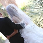 Back view of bride wearing a veil embracing groom