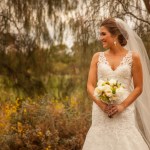 Bride smiling and holding flowers in front of a willow tree on golf course