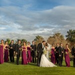 Wedding party on golf course as bride and groom kiss