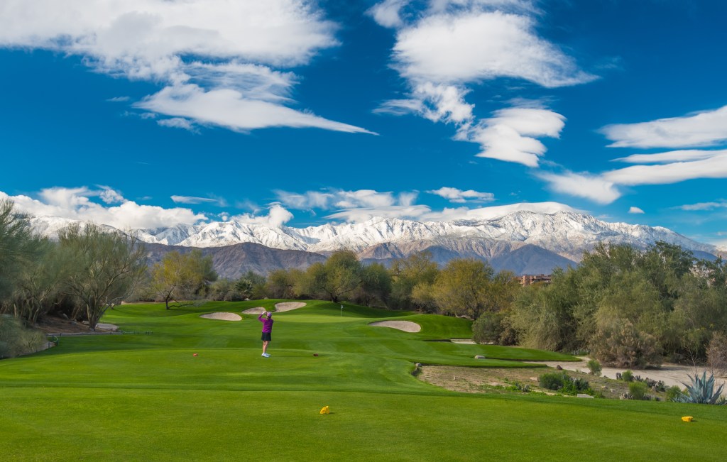 Golfer playing a round at Desert Willow Golf Resort with snow-capped mountains in the background, highlighting exclusive discount offers for additional rounds.