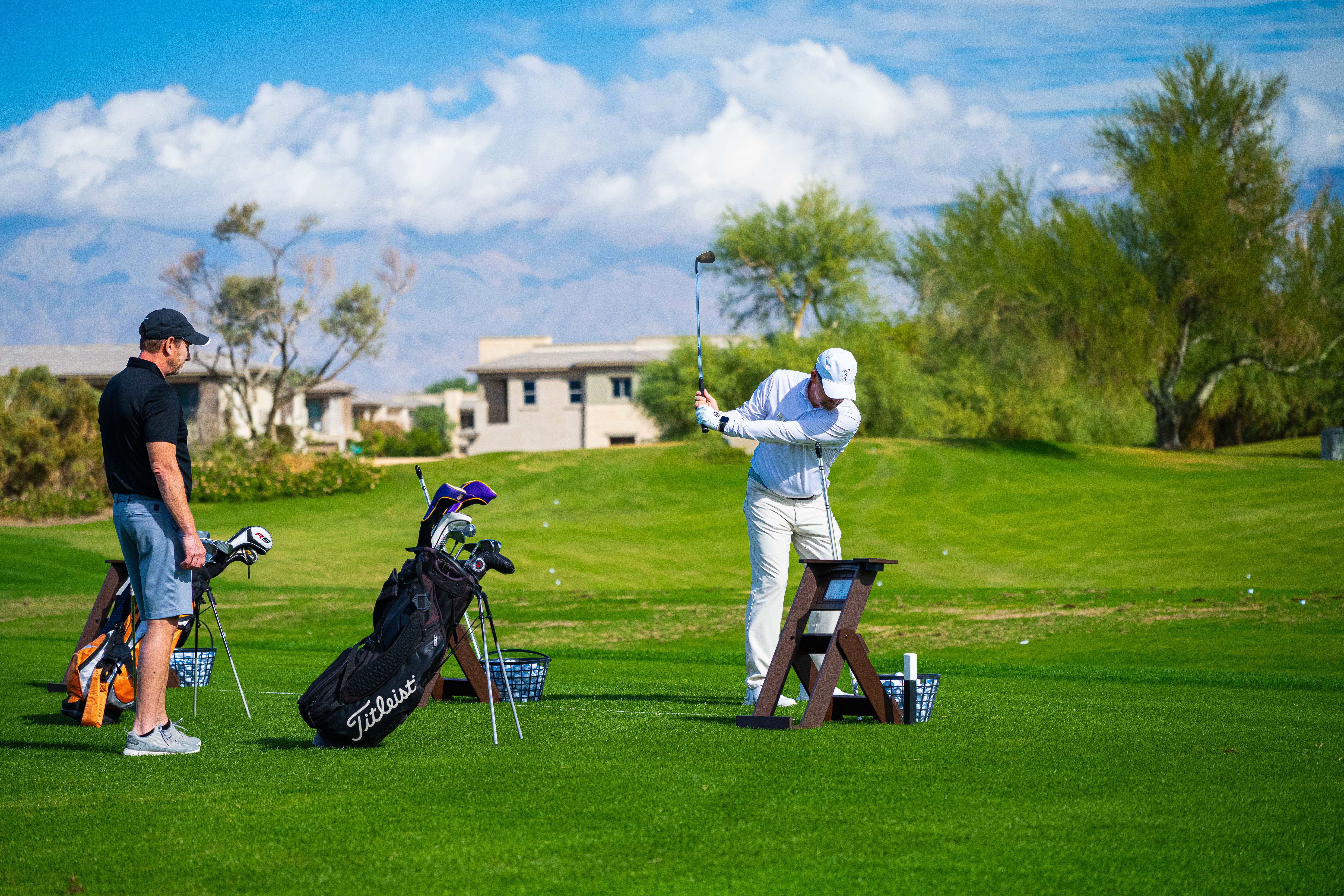 Golf students practicing at Palm Desert Golf Academy with golf bags and clubs on the range, featuring a customer testimonial praising PGA Professional Paul Bucy for his patient and helpful coaching, with scenic desert mountains in the background.