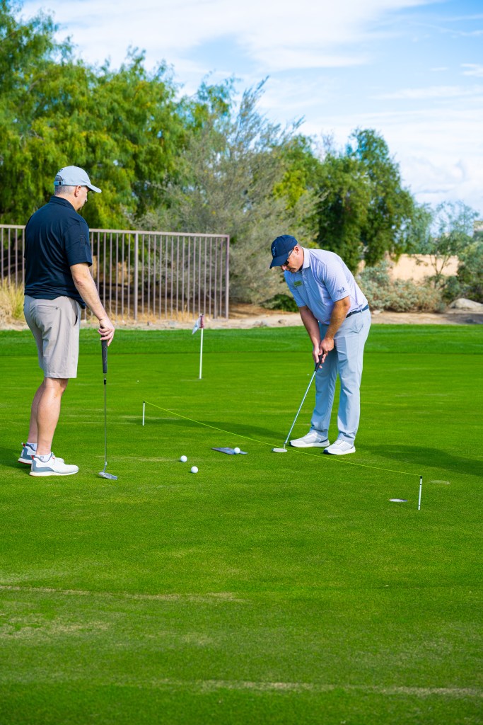 Golf instructor demonstrating putting techniques to a student on the practice green during the Mastering the Short Game Golf School at Palm Desert Golf Academy.