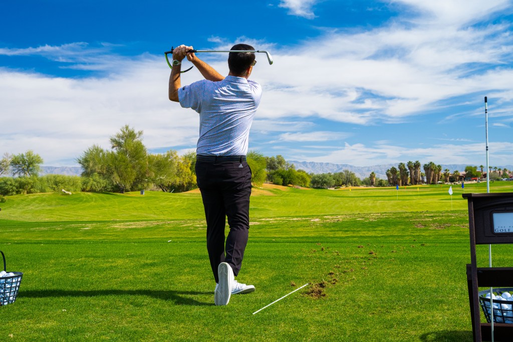 Golfer hitting an iron shot on the practice range at the Palm Desert Golf Academy at Desert Willow Golf Resort, promoting exclusive practice facility access available through Academy memberships.