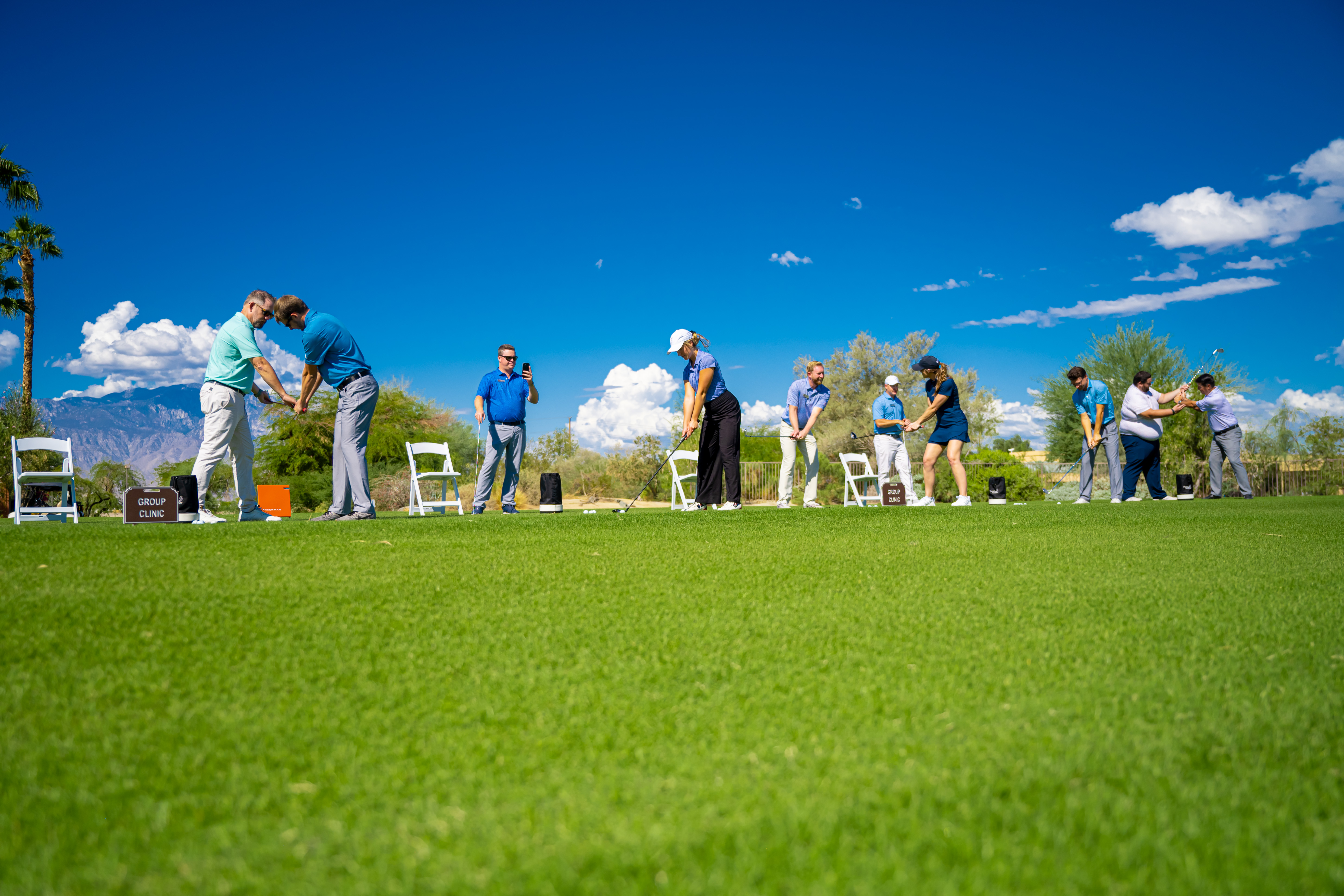 Golf instructor teaching a group of beginners during the Get Golf Ready program at Palm Desert Golf Academy, with stunning desert mountains in the background and a banner promoting enrollment.