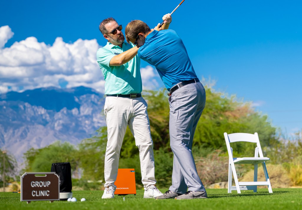 Golf instructor helping a beginner with swing fundamentals during the Get Golf Ready program at Palm Desert Golf Academy, with mountains in the background.