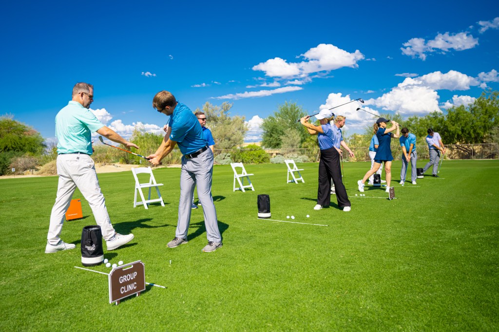 Golfers participating in a daily golf clinic at the Palm Desert Golf Academy at Desert Willow Golf Resort, receiving one-on-one instruction and practicing full swings on the grass range under clear desert skies.