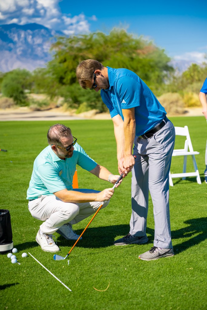 PGA golf instructor guiding a student’s grip during a one-on-one lesson at the Palm Desert Golf Academy, with bright green turf and desert landscape in the background