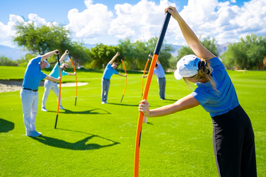 Golfers participating in a Palm Desert Golf Academy Stick Mobility Golf Fitness class at Desert Willow Golf Resort, using mobility sticks to improve flexibility, strength, and swing performance on the practice range.
