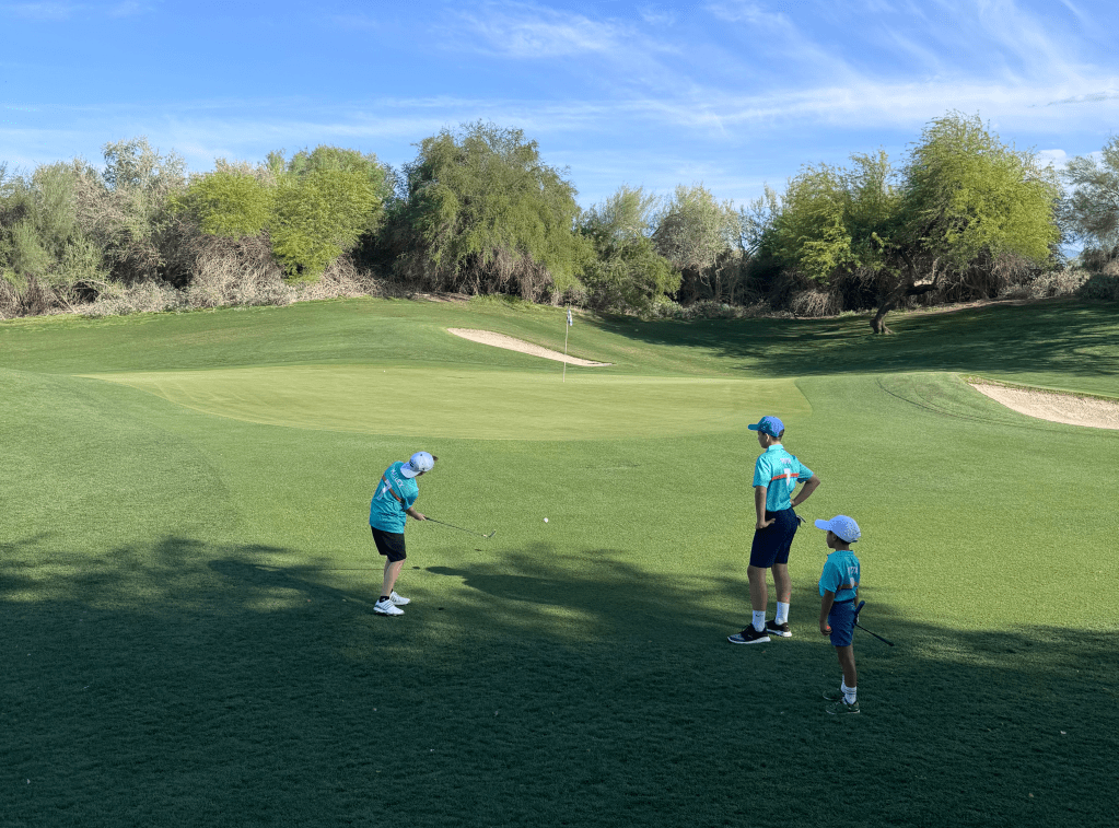 Junior golfers receiving instruction during a Palm Desert Golf Academy PGA Jr. League session at Desert Willow Golf Resort, practicing short game skills on the green under coach supervision.