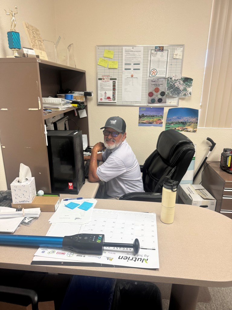 Assistant Superintendent Raul Melero sitting at his desk in the Desert Willow Golf Resort maintenance office, reflecting on his 29-year career in golf course management.